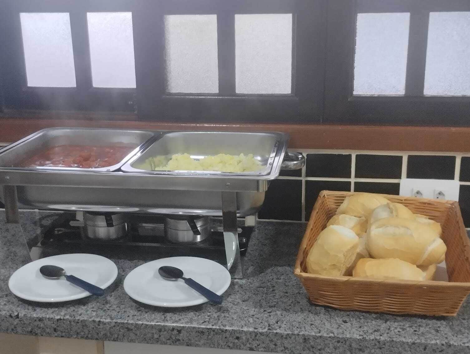 Un buffet composé de deux plats de service, l’un contenant une sauce rouge et l’autre un aliment de couleur jaunâtre, ainsi qu’un panier de pain posé sur un comptoir en granit.