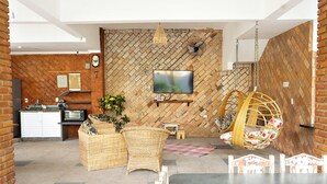 Uma sala de estar moderna com parede de tijolos, televisão de tela plana, móveis de vime e uma cadeira suspensa.