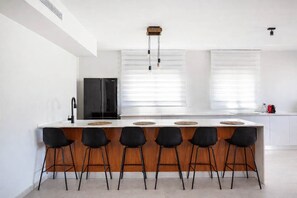 Una cocina moderna con una isla central, taburetes negros, un refrigerador negro y una ventana con persianas.