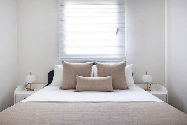 Un dormitorio ordenado con una cama grande, dos mesitas de noche y una ventana con persianas.