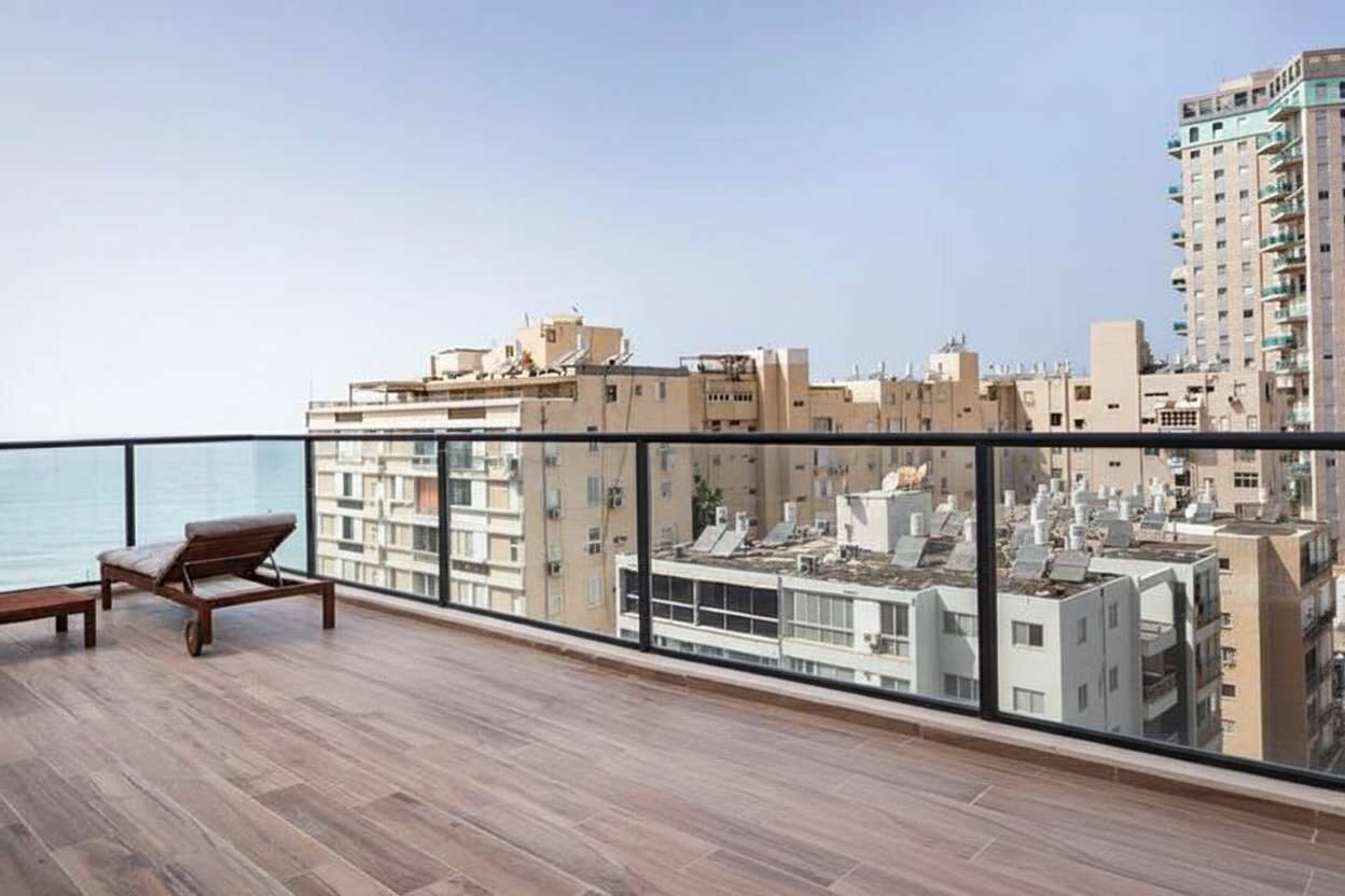 A balcony with a wooden floor, a lounge chair, and a view of a cityscape with buildings and a body of water.
