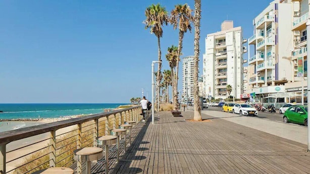 A wooden boardwalk with benches, palm trees, and a view of the ocean. - Beachside 3BR | Huge Patio| Mamad (Bat Yam)