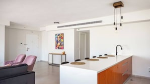 A modern kitchen with a central island, a dining area with chairs, and a living space with a sofa. - Beachside 3BR | Huge Patio| Mamad (Bat Yam)