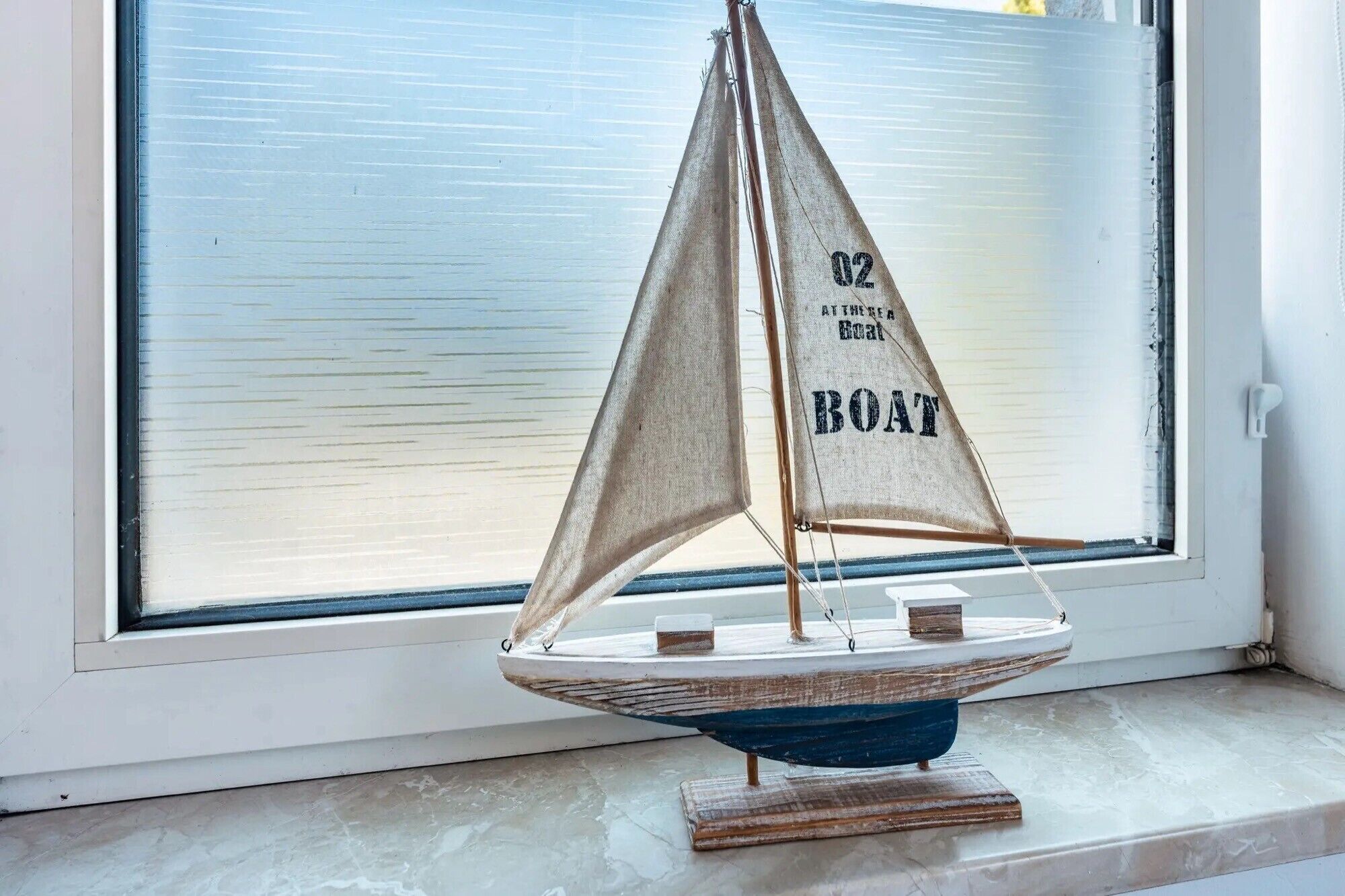 Un velero modelo con la inscripción '02 BOAT' en la vela, expuesto en un alféizar.