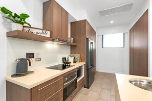 A modern kitchen with wooden cabinets, a stainless steel refrigerator, and a built-in oven. - Sensational Swim Out—Resort Living by the Sea (Palm Cove)