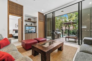 A modern living room with a glass door leading to an outdoor patio, a flat-screen TV, and a wooden coffee table. - Orchid at Temple Resort: A Swim-out Tropical Oasis (Palm Cove)