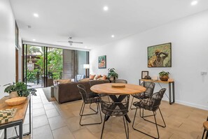 A modern living room with a dining area, large windows, and a ceiling fan. - Sensational Swim Out—Resort Living by the Sea (Palm Cove)