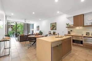 A modern kitchen with a central island, built-in oven, and a dining area with a view to the outdoors. - Sensational Swim Out—Resort Living by the Sea (Palm Cove)