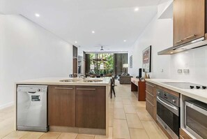 A modern kitchen with a dishwasher, double sink, and built-in oven. - Orchid at Temple Resort: A Swim-out Tropical Oasis (Palm Cove)