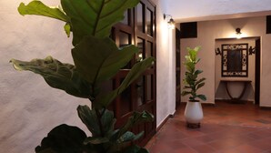 A hallway with a potted plant, a wooden door, and a wall-mounted light fixture. - Hotel Prados de la Serranía (Lebrija)
