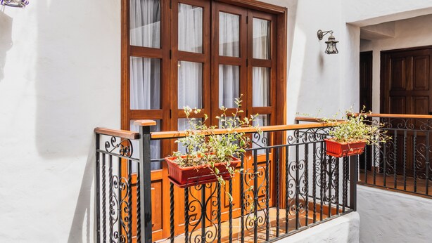 A balcony with wrought iron railings, wooden doors, and potted plants. - Hotel Prados de la Serranía (Lebrija)