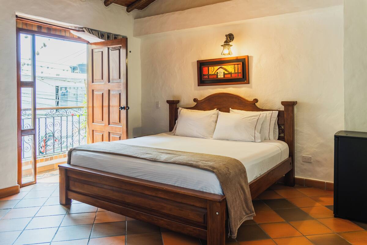 A bedroom with a wooden bed, a nightstand, and a wall-mounted light fixture.