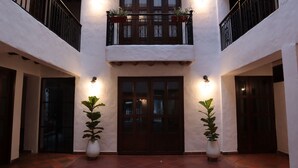 A courtyard with a central door flanked by two potted plants, a balcony with railings, and a white wall with a window. - Hotel Prados de la Serranía (Lebrija)