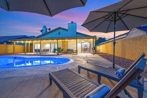 A backyard with a swimming pool, lounge chairs, and umbrellas.