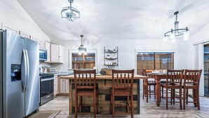 Moderni keittiö, jossa on ruostumattomasta teräksestä valmistetut kodinkoneet, puukaapit ja keskellä oleva saareke, jonka ympärillä on tuoleja.