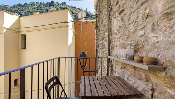 Un balcone con tavolo e sedie in legno, un muro in pietra e vista su un pendio.
