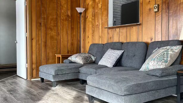 A modern living room with a grey sectional sofa, wooden panel walls, a large mirror, and a floor lamp. - Beautifully renovated spacious home in Mishawaka (Mishawaka)