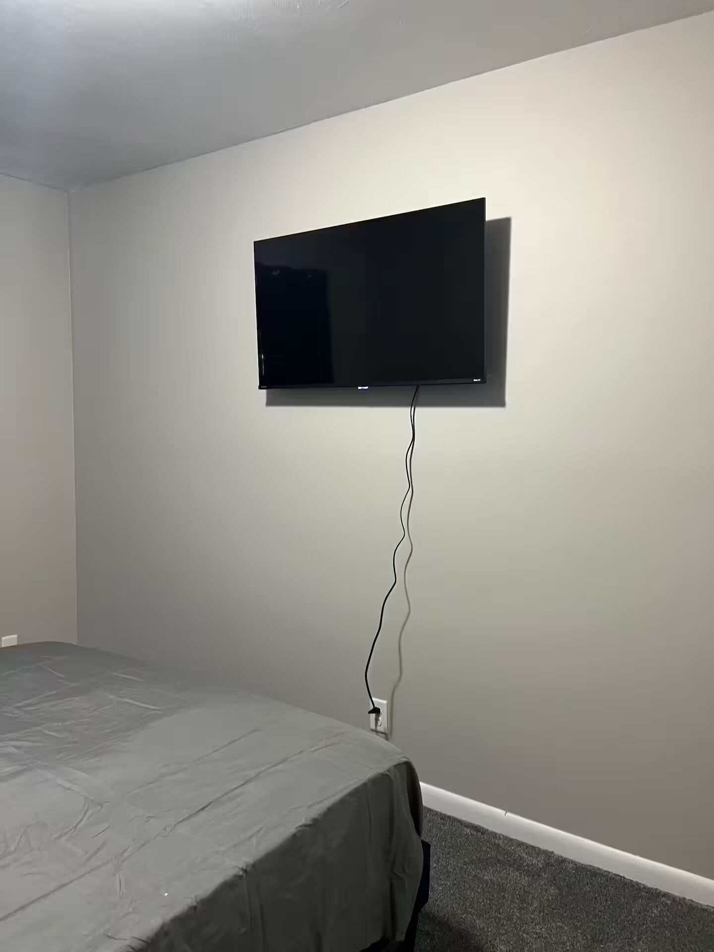 A room with a bed, a mounted flat-screen TV, and a power outlet on the wall.