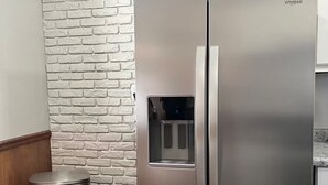 A stainless steel Whirlpool refrigerator with a water and ice dispenser, positioned next to a white brick-patterned wall and a wooden floor. - Beautifully renovated spacious home in Mishawaka (Mishawaka)