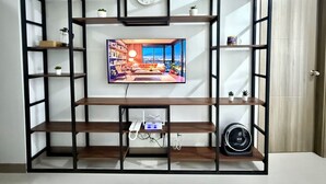 A living room with a TV mounted on a black-framed wall, surrounded by wooden shelves, a clock, and a fan. - S Residences MOA by darpm (Pasay)