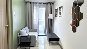 A modern, well-lit room with a grey sofa, a small black table, and a decorative wall piece. - S Residences MOA by darpm (Pasay)