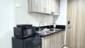 A compact kitchen with a black refrigerator, a microwave, a kettle, and a sink. - S Residences MOA by darpm (Pasay)