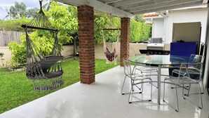 Un patio con una mesa y sillas de vidrio, una silla colgante y un pilar de ladrillo.