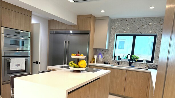 Una cocina moderna con electrodomésticos de acero inoxidable, una isla central con fruta, armarios de madera y un ventanal con vistas.