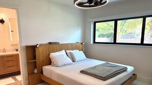 Un dormitorio moderno con estructura de cama de madera, ropa de cama blanca y ventana con vista a la vegetación.