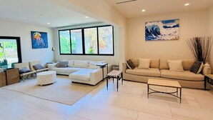 Un salón amplio con un sofá blanco, un sofá beige, una mesa de centro y un ventanal con vistas a zonas verdes.