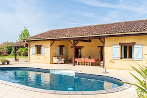 Een huis met een zwembad, een overdekt terras en een eethoek.