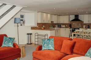 A modern kitchen with white cabinets, a central island, and a dining area with a white table and chairs. - Willoughby Cottage - Rustic Retreat in Crieff (Muthill)