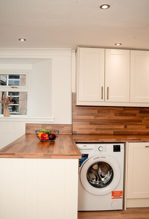 A kitchen with wooden countertops, a washing machine, and cabinets. - Willoughby Cottage - Rustic Retreat in Crieff (Muthill)