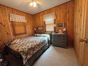 A bedroom with a bed, dresser, and two windows with blinds.