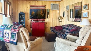 Une pièce chaleureuse avec des murs en bois, un buffet rouge, un canapé bleu et blanc, un fauteuil beige et une petite table.