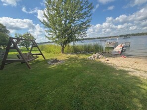 A grassy area with a swing set, a tree, and a dock extending into a lake with boats.