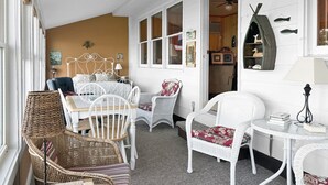 Une pièce chaleureuse, meublée de meubles en osier, avec un lit doté d’une tête de lit blanche et une petite table sur laquelle sont posés des livres.