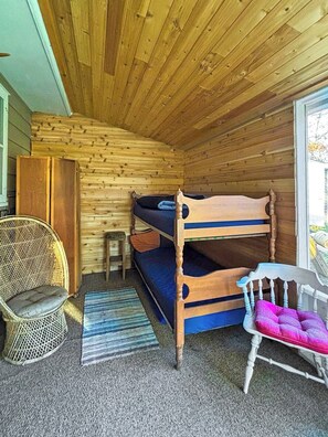 Une petite pièce agréable et chaleureuse, avec un lit superposé, une chaise en osier, une petite table et une fenêtre.