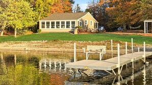 Une maison avec un quai s’avançant dans un lac paisible, entourée d’arbres aux feuilles d’automne.