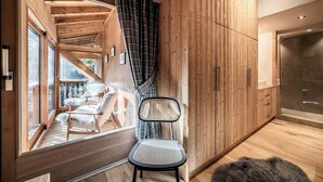 A wooden interior with a chair, a glass shower, and a view of an outdoor deck. - Snowdust – Warm & Welcoming Stay in Megève (Megeve)