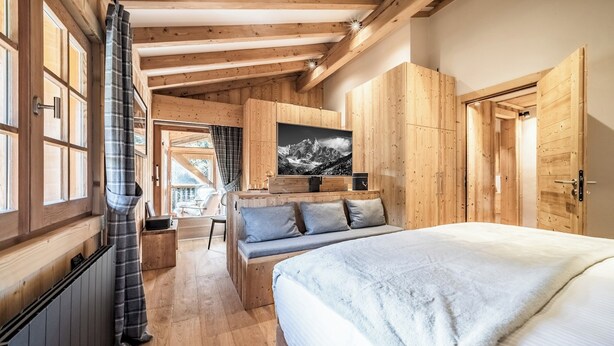 A wooden cabin-style bedroom with a large bed, a seating area, and a mountain view. - Snowdust – Warm & Welcoming Stay in Megève (Megeve)