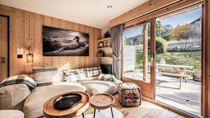 A cozy bedroom with a large window, wooden walls, a bed with striped bedding, a fireplace, and a view of the outdoors. - Snowdust – Warm & Welcoming Stay in Megève (Megeve)