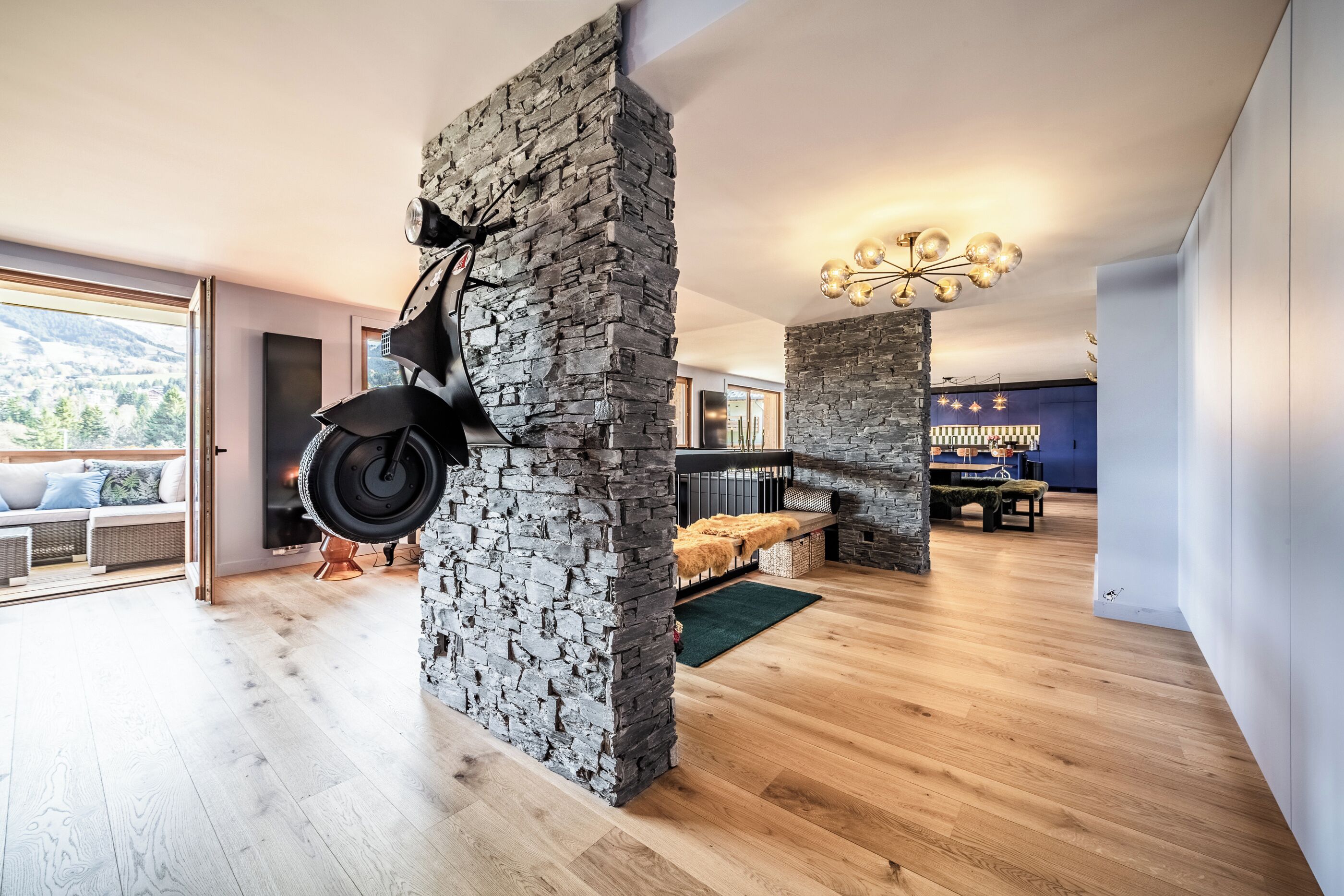 A modern interior with a stone wall, wooden flooring, and a hanging light fixture.