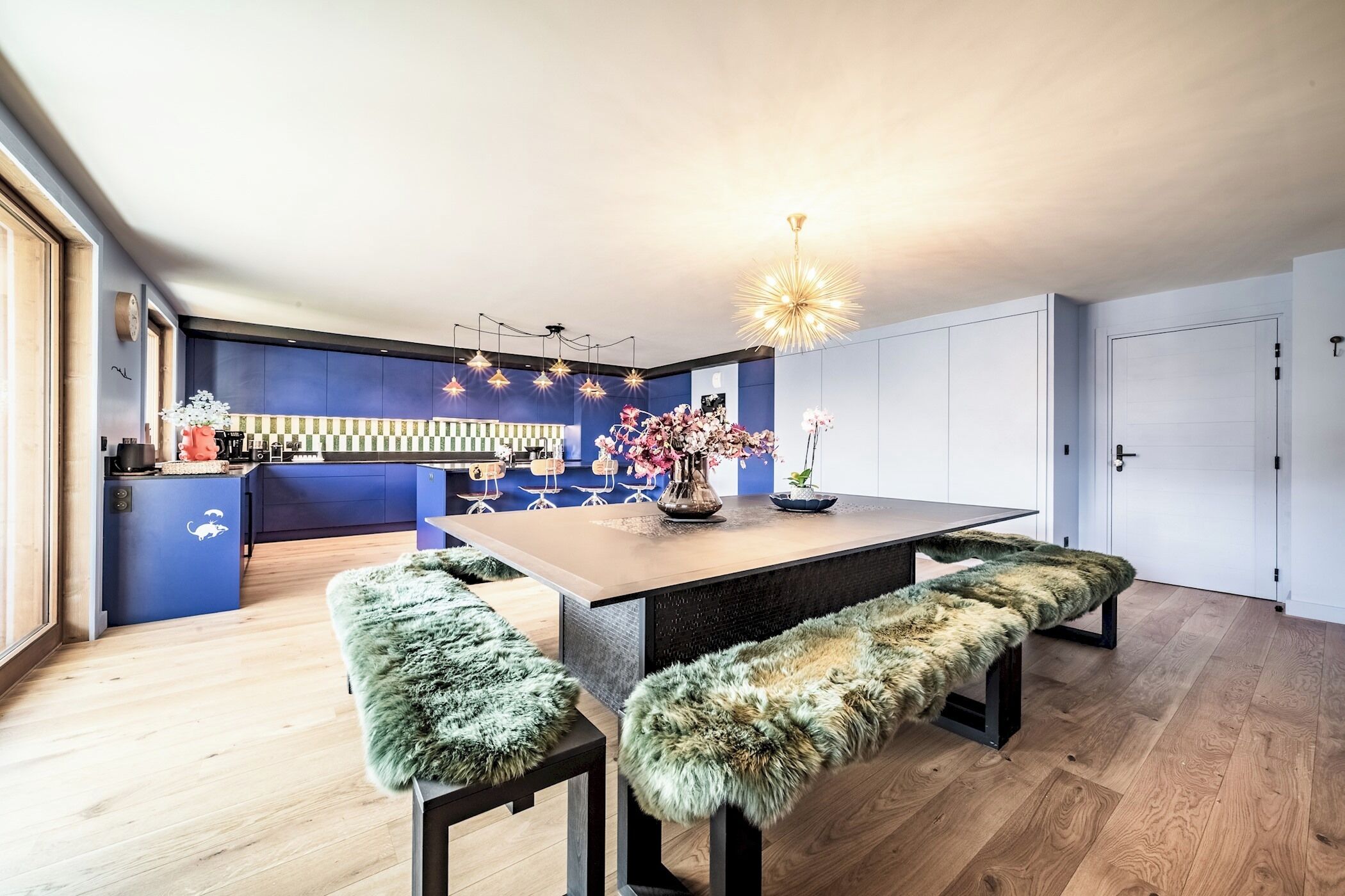 A modern kitchen with a central island, bar stools, and a chandelier.