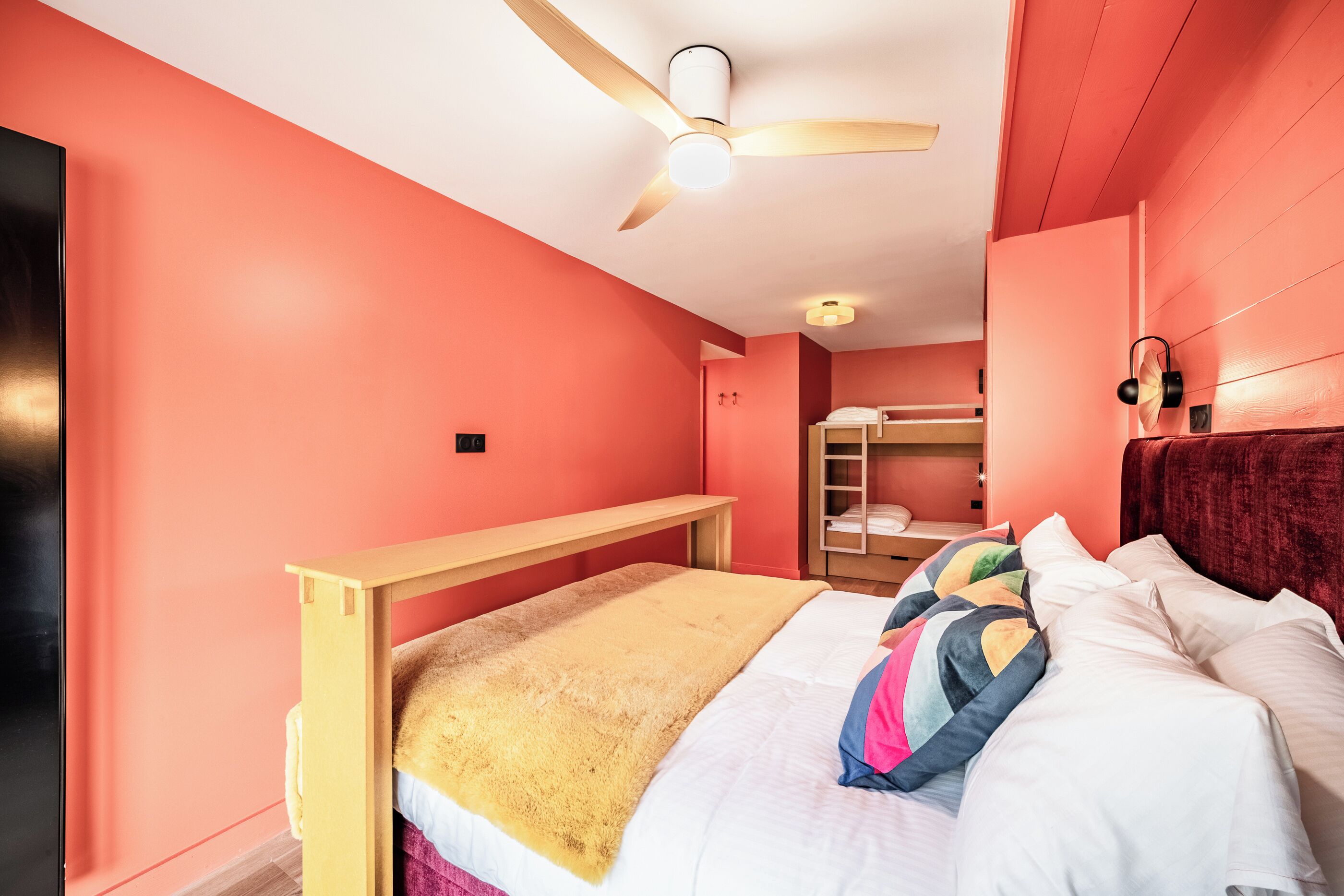 A bedroom with a bunk bed, a ceiling fan, and a red wall.