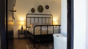 Un dormitorio con estructura de cama metálica, dos lámparas de noche, un cesto de ropa blanca y una alfombra estampada.