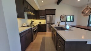 A modern kitchen with dark cabinetry, stainless steel appliances, and a large island with a sink. - Snowcreek Resort Vacation Rental 1543 (Mammoth Lakes)