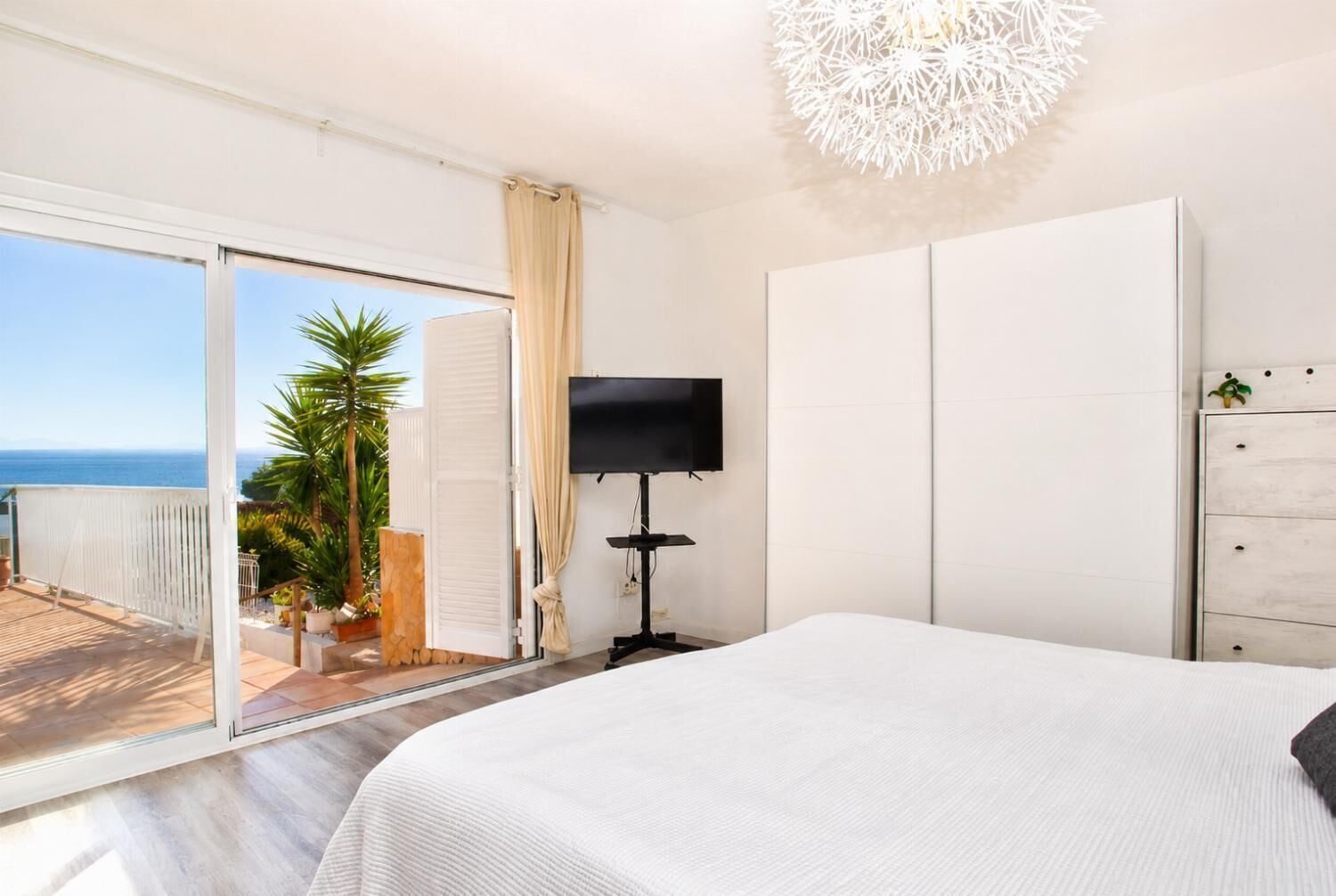 A bedroom with a bed, a TV, a wardrobe, and a balcony with a view of the sea.