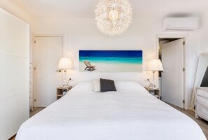 Ein Hotelzimmer mit einem großen Bett, zwei Nachttischen mit Lampen, einer Deckenleuchte und einem Wandbild im Strandhausstil.