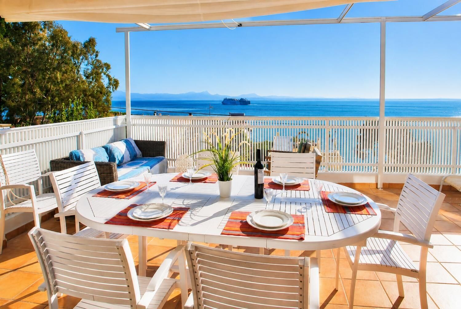 Un espace de restauration en plein air avec vue sur la mer, doté de mobilier blanc et d’une table dressée pour deux personnes.